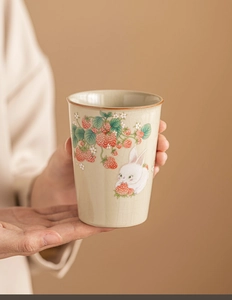 Close-up of hand-held Ru kiln ceramic tea cup with hand-painted strawberry and rabbit motif