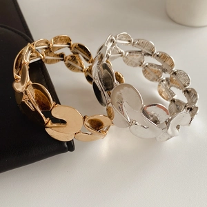 Detail of gold and silver S-shaped metal bracelets on textured black leather and white table