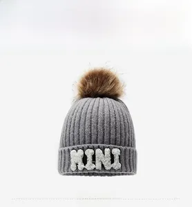 Detail of gray ribbed knit beanie with brown faux fur pom-pom and white MINI letter patch
