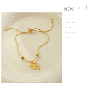 Detailed view of a gold heart charm bracelet on a ceramic tray with adjustable pull clasp