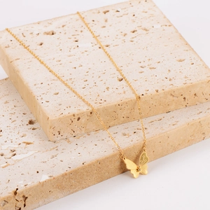 Élégant collier pendentif papillon doré exposé sur des blocs de pierre texturés