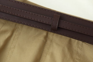 Détail macro d'une ceinture en cuir marron avec double surpiqûre sur tissu sergé kaki
