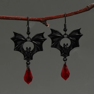Detailed view of Gothic black bat earrings with red teardrop crystals on a natural branch