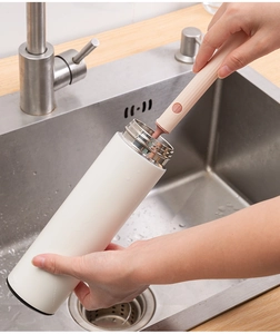 Close-up of pink long-handle sponge brush cleaning a white insulated bottle in a kitchen sink