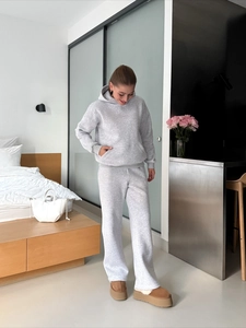 Women's grey two-piece tracksuit with hoodie and wide-leg pants in a modern home setting