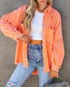 Detail of frayed tassels and silver metal buttons on a loose orange denim jacket