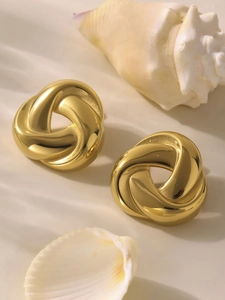Detailed shot of golden twisted hoop earrings on beige surface with decorative shells
