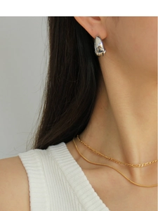 Detail of silver teardrop hoop earrings paired with layered gold chains on model
