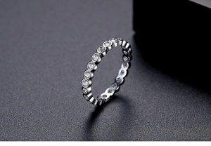 Macro shot of silver ring with embedded round clear zircons on a dark textured surface