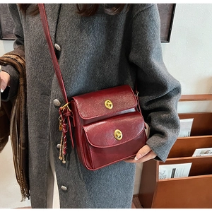 Detail of burgundy leather crossbody bag with dual flaps and gold twist lock on coat