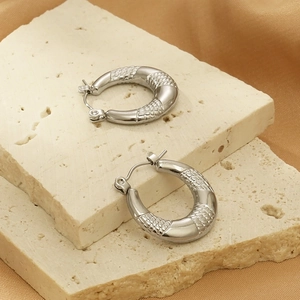 Close-up of silver hoop earrings with snake skin texture on a natural stone base