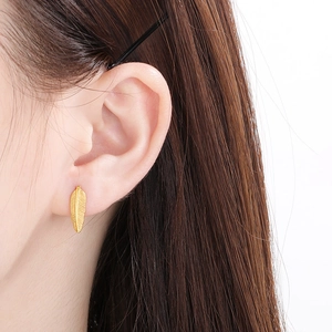 Close-up of a golden feather earring worn on ear showing detailed metal texture