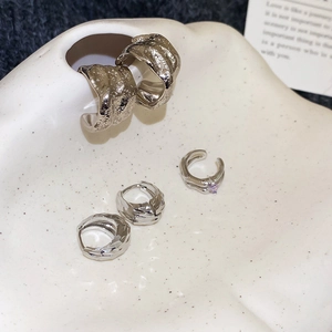 Silver C-shaped hoop earrings with lava texture and purple zircon ear cuff on ceramic tray