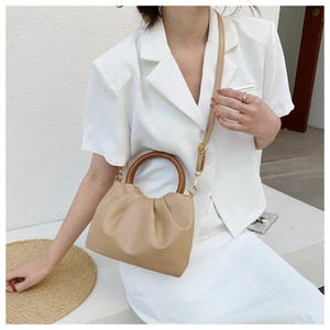 Detail of beige pleated cloud bag featuring a round wooden handle and adjustable strap