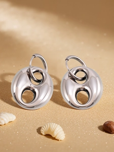 Close-up of geometric hollow metal earrings with polished mirror finish on natural sand