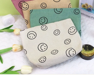 Detail of corduroy makeup bags in pastel colors featuring a minimalist black smiley face