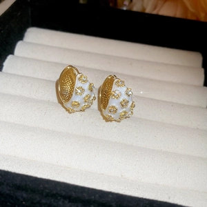 Macro shot of gold-plated huggie earrings with white enamel flowers and crystals