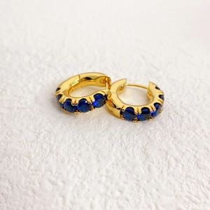 Macro detail of gold hoop earrings featuring inlaid round navy blue zircon gemstones