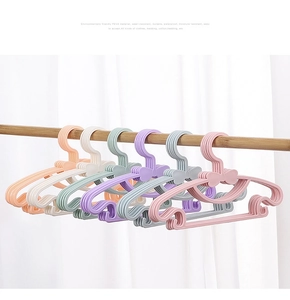 Pastel bow-shaped children's hangers with anti-slip grooves on a wooden clothes rail
