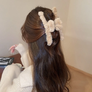 Close-up of beige plush bow hair claw clip worn on long hair in a cozy lifestyle setting