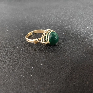 Detailed macro view of handmade gold wire-wrapped ring with a green gemstone bead