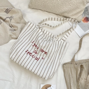 Detailed close-up of striped canvas tote bag with smile face and red embroidered slogan