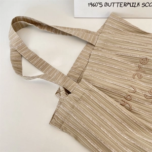 Close-up of beige striped canvas tote bag with brown you are letter embroidery detail