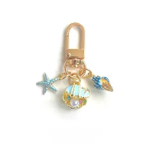 Detail of ocean-themed keychain with starfish, seashell, and pearl on gold ring