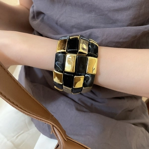 Macro shot of gold and black checkered acrylic bangle on wrist with a polished finish