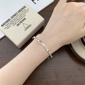 Detail showing irregular wavy silver cuff bracelet on wrist with textured liquid metal style