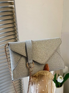 Silberne Glitzer-Umschlagtasche mit goldener Kette vor neutralem Innenraum-Hintergrund
