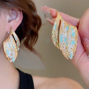 Detailed macro shot of gold textured leaf earrings with blue and white enamel splash effect