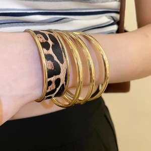 Detailed close-up of a leopard print leather cuff paired with gold stacking bangles