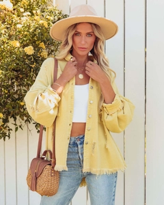 Detail shot of yellow denim jacket with raw hem edges and frayed cuff texture on model