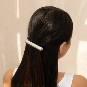 Minimalist silver cylindrical metal hair tie clip on long dark hair against beige background