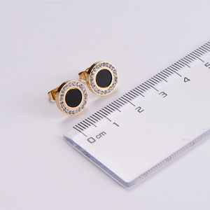 Close-up of gold and black stud earrings with cubic zirconia inlay and ruler for scale