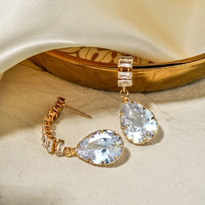 Elegant gold drop earrings with pear-cut cubic zirconia on a silk display background