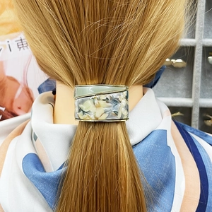 Close-up of a geometric hair tie with gold frame and green marble texture acetate detail