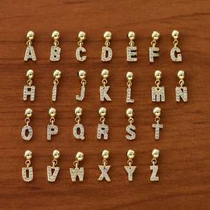 Set of 26 gold alphabet pendants with sparkling zircon stones on wood background