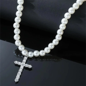 Detail of faux pearl necklace with iced-out rhinestone cross pendant on black surface