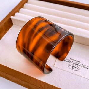 Macro detail of wide open cuff bracelet featuring amber tortoiseshell texture on velvet