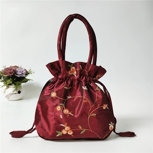 Detail showing the burgundy silk texture and floral embroidery on the drawstring bucket bag
