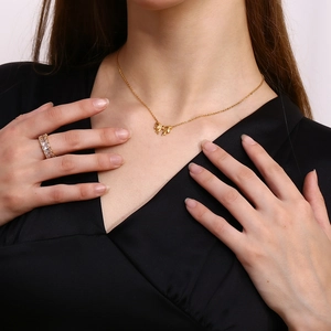Close-up of 18k gold ribbon bow pendant necklace and square crystal ring on model