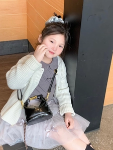 Close-up of a child wearing the black glossy leather crossbody bag with gold air lettering