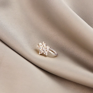 Macro shot of silver flower ear cuff with sparkling zircon stones on silk fabric