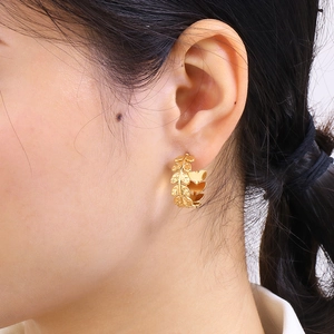Detail shot of a model wearing the gold leaf-shaped titanium steel hoop earring