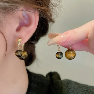 Détail de boucles d'oreilles en perles œil de tigre brun avec liens en or sur modèle