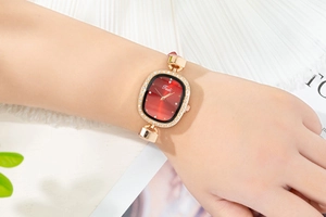 Detail of elegant gold-tone oval watch with red dial and rhinestone-set bezel on wrist