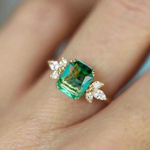 Detail of a gold ring with a green rectangular gemstone and marquise-cut zircon accents