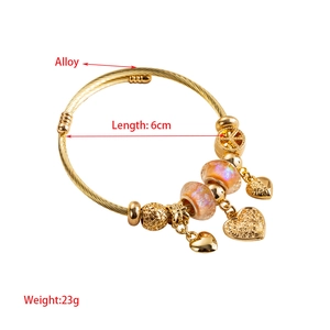 Golden alloy charm bracelet with heart pendants and textured beads on white background